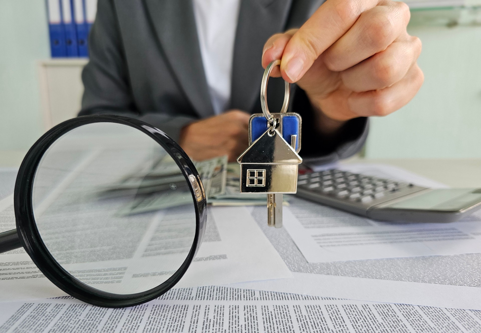 Agente de bienes raíces que presenta las llaves de la casa con calculadora y documentos en la oficina