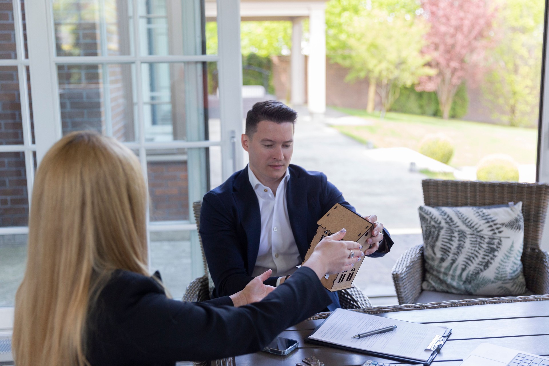 Comprador atento sostiene casa de madera en miniatura con agente de bienes raíces